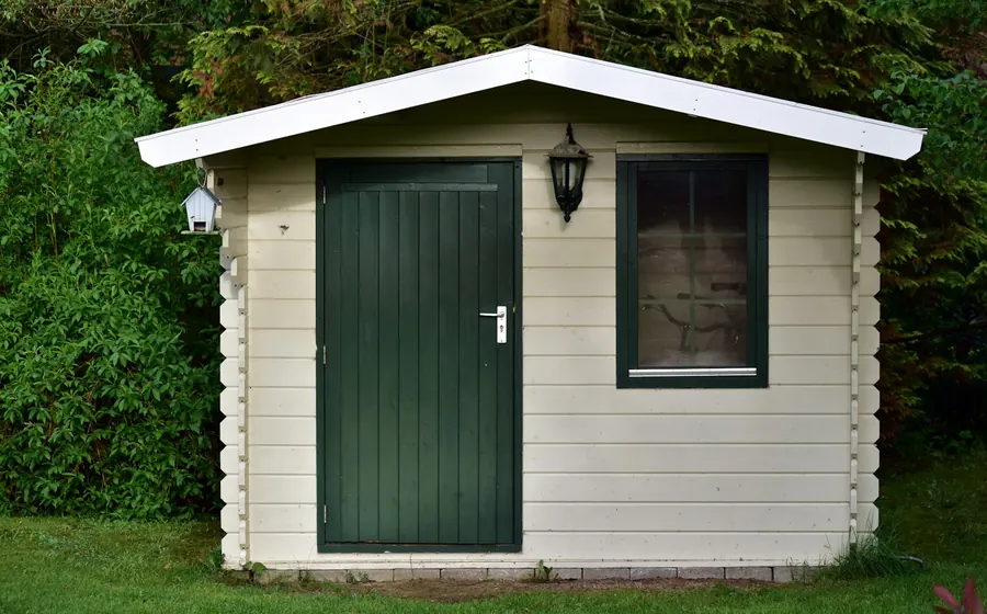 Bodega prefabricada de madera con puerta verde en un jardín